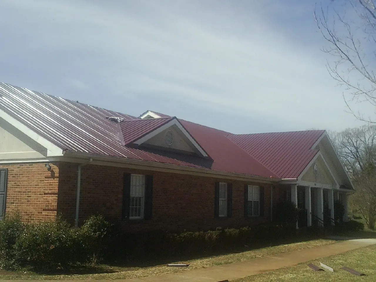 Red metal roof with gabled entries on a long brick building, from a Hail Damage Roof Repair job in Ocilla