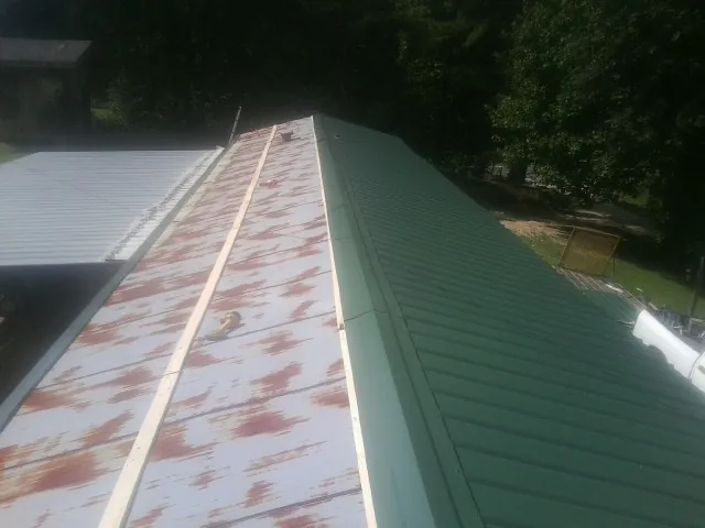 Old rusted panels beside newly installed green metal roofing — Wind Damage Roof Repair by Roofing Brothers in Ocilla