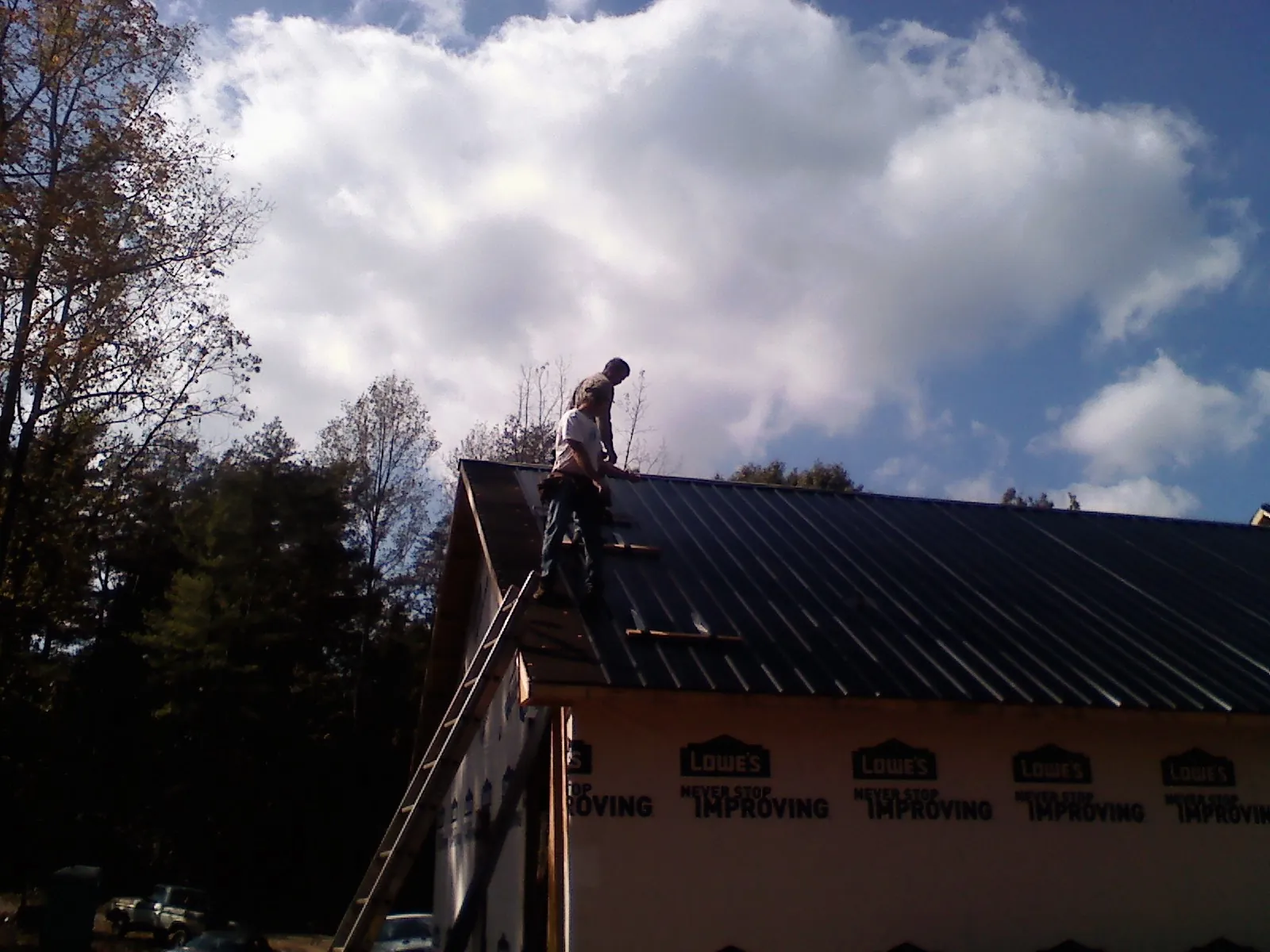 Roofer fastening dark metal panels high against a cloudy sky, from a Roof Inspection job in Ocilla